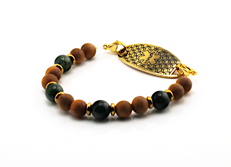 A beaded bracelet featuring matte brown cedar wood beads, polished dark green beads, and a gold-toned medical ID tag with an engraved geometric pattern, displayed on a clean white background.